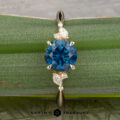 The "Iris" ring in 14K yellow gold, set with a 1.60-carat Montana sapphire and four white accent stones, rests on a green leaf; the Earth's Treasury logo is shown below.