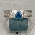 The "Shannon" ring in 14K white gold features a 0.92-carat Montana sapphire and detailed Celtic knotwork, shown upright on a rough-textured greenish stone.