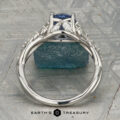The "Yulania" ring showcases a platinum band with a 1.52-carat Ceylon sapphire center, accented by marquise white stones, displayed on a rough blue-green stone background.