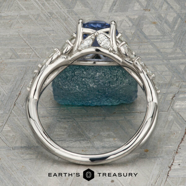 The "Yulania" ring in platinum with 1.52-carat Ceylon sapphire The "Yulania" ring showcases a platinum band with a 1.52-carat Ceylon sapphire center, accented by marquise white stones, displayed on a rough blue-green stone background.