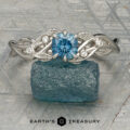 The “Viney” ring in platinum, featuring a 0.99-carat Montana sapphire and diamond accents, is displayed on a raw blue stone atop a textured surface with the "Earth's Treasury" logo below.