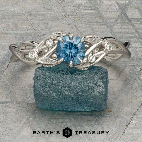 The “Viney” ring in platinum with 0.99-carat Montana sapphire The “Viney” ring in platinum, featuring a 0.99-carat Montana sapphire and diamond accents, is displayed on a raw blue stone atop a textured surface with the "Earth's Treasury" logo below.