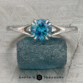 The Marlowe ring with a round blue gemstone stands upright on a rough blue stone, set against a textured gray background. The text "Earth's Treasury" appears at the bottom.