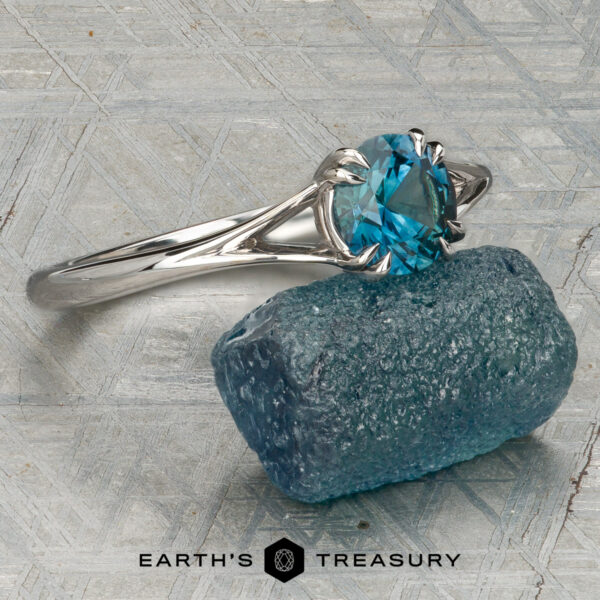 The Marlowe Ring The Marlowe Ring featuring a blue gemstone, stacked from 53 images using Method=B (R=14, S=2), rests on a rough blue stone atop a textured surface with the Earth's Treasury logo below.
