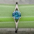 The Marlowe ring featuring a round blue gemstone in a platinum prong setting, shown on a green background with the "Earth's Treasury" logo at the bottom.