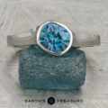 A platinum “Winona” ring with a 1.21-carat Montana sapphire rests on a textured blue stone, displayed on a patterned surface with the text "Earth's Treasury" below.