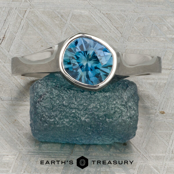 The “Winona” ring in platinum with 1.21-carat Montana sapphire A platinum “Winona” ring with a 1.21-carat Montana sapphire rests on a textured blue stone, displayed on a patterned surface with the text "Earth's Treasury" below.