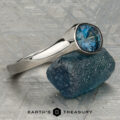 A platinum “Winona” ring with a 1.21-carat Montana sapphire rests on a textured blue stone, displayed on a patterned surface with the text "Earth's Treasury" below.