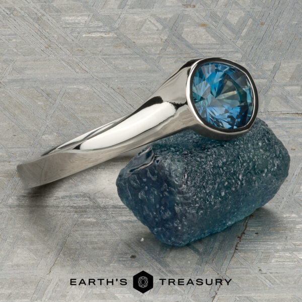 The “Winona” ring in platinum with 1.21-carat Montana sapphire A platinum “Winona” ring with a 1.21-carat Montana sapphire rests on a textured blue stone, displayed on a patterned surface with the text "Earth's Treasury" below.