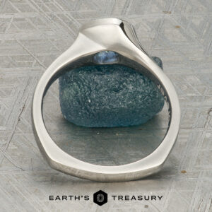 A platinum “Winona” ring with a 1.21-carat Montana sapphire rests on a textured blue stone, displayed on a patterned surface with the text "Earth's Treasury" below.