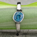 A platinum “Winona” ring with a 1.21-carat Montana sapphire rests on a textured blue stone, displayed on a patterned surface with the text "Earth's Treasury" below.