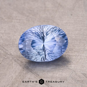 Close-up of a 1.48-Carat Ceylon Sapphire with intricate facets and an oval shape in light blue, resting on a textured surface.