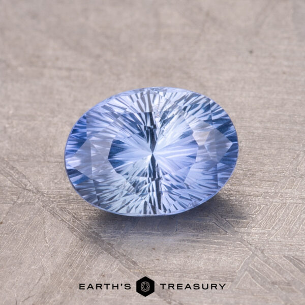 1.48-Carat Ceylon Sapphire Close-up of a 1.48-Carat Ceylon Sapphire with intricate facets and an oval shape in light blue, resting on a textured surface.