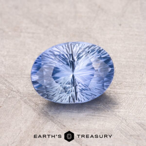 Close-up of a 1.48-Carat Ceylon Sapphire with intricate facets and an oval shape in light blue, resting on a textured surface.