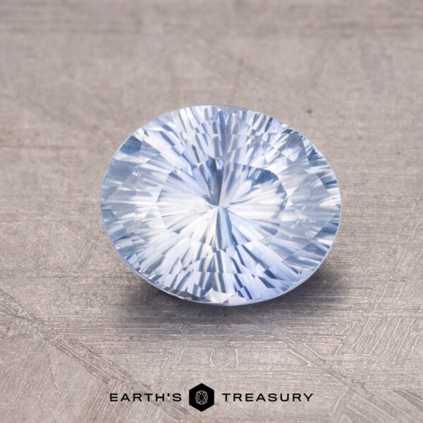 1.54-Carat Ceylon Sapphire A 1.54-carat Ceylon Sapphire, round and light blue with a faceted surface, rests on a textured gray background with the text "Earth's Treasury" beneath it.