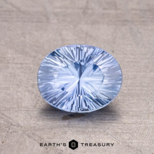 A 1.31-carat Ceylon Sapphire, blue and round with intricate facets, rests on a textured surface.