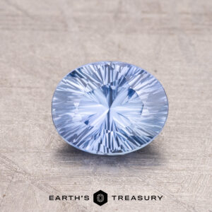 A 1.31-carat Ceylon Sapphire, blue and round with intricate facets, rests on a textured surface.