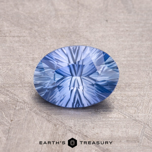 1.06-Carat Ceylon Sapphire A 1.06-carat Ceylon Sapphire, round and faceted with intricate patterns on its textured blue surface, features Earth's Treasury's logo at the bottom.