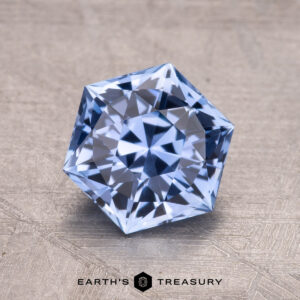 A 2.03-carat Ceylon sapphire set on a textured gray background with "EARTH'S TREASURY" displayed beneath it.