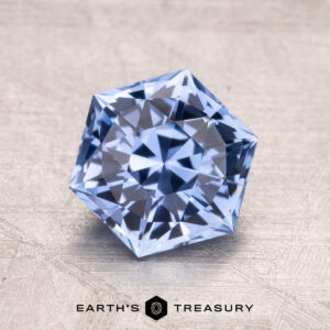 A 2.03-carat Ceylon sapphire set on a textured gray background with "EARTH'S TREASURY" displayed beneath it.