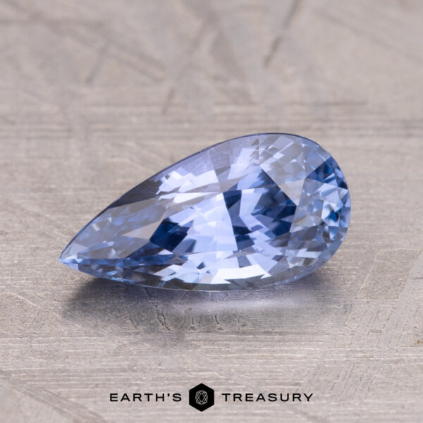 1.69-Carat Ceylon Sapphire A 1.69-carat Ceylon Sapphire, pear-shaped and faceted in blue, is showcased on a textured surface with the "Earth's Treasury" logo at the bottom.