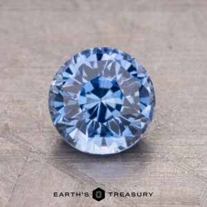 A 1.62-carat Ceylon Sapphire, round and faceted, is showcased on a textured surface.