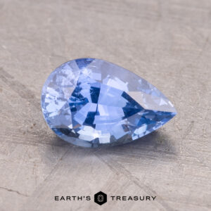 A 1.57-carat pear-shaped Ceylon sapphire rests on a textured gray surface with the "Earth's Treasury" logo at the bottom.