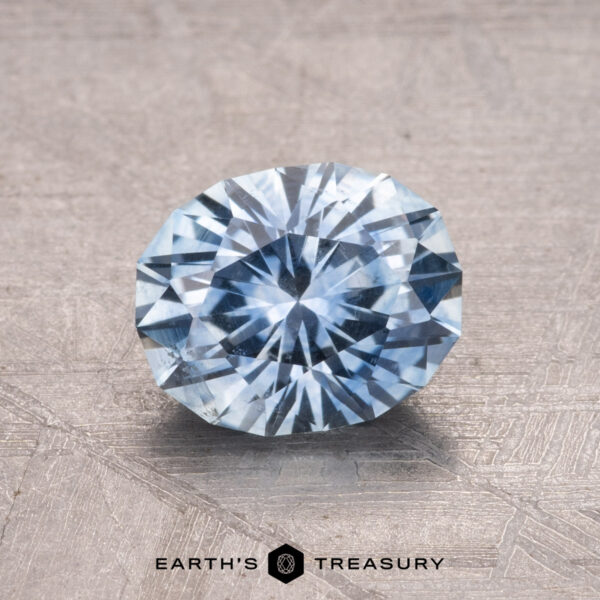 1.78-Carat Montana Sapphire (Heated) A round, faceted Light Sky Blue 1.78-Carat Montana Sapphire (Heated) sits on a textured gray surface. Label: "Earth's Treasury.