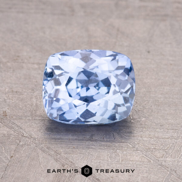 1.45-Carat Ceylon Sapphire A 1.45-carat Ceylon Sapphire with a cushion cut, light blue hue rests on a textured gray surface.