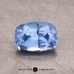 A 1.68-carat Ceylon sapphire (heated) in a cushion cut is set on a textured surface, displaying the "Earth's Treasury" logo beneath it.