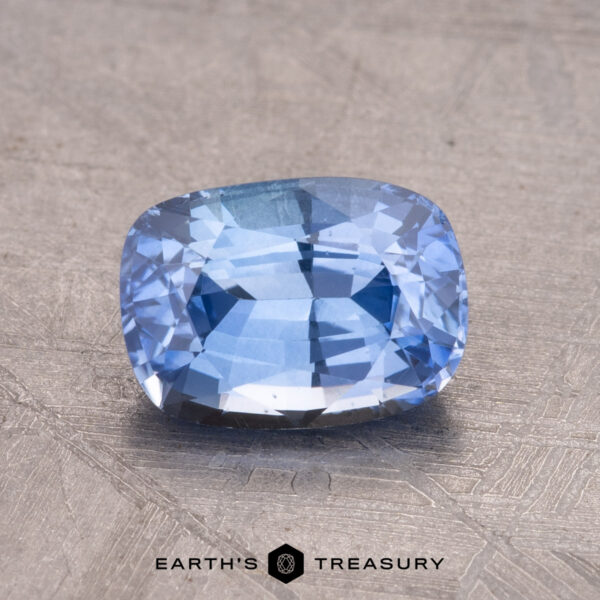 1.68-Carat Ceylon Sapphire (Heated) A 1.68-carat Ceylon sapphire (heated) in a cushion cut is set on a textured surface, displaying the "Earth's Treasury" logo beneath it.
