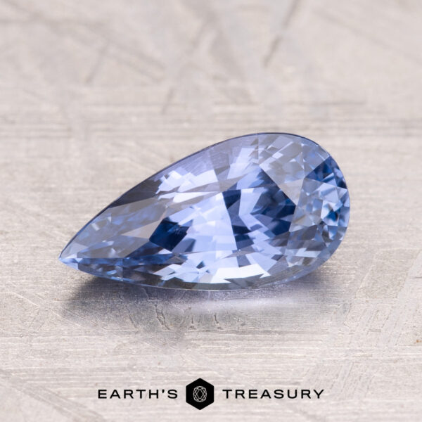 1.69-Carat Ceylon Sapphire A 1.69-carat Ceylon Sapphire, pear-shaped and faceted in blue, is showcased on a textured surface with the "Earth's Treasury" logo at the bottom.
