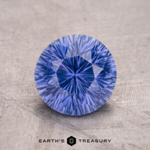 A 2.05-carat Ceylon Sapphire, round and faceted with a lavender hue, placed on a textured surface.