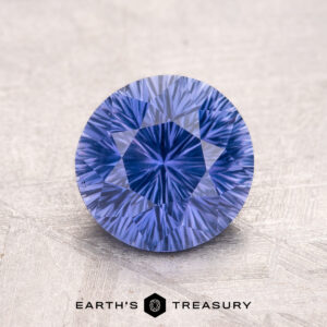 A 2.05-carat Ceylon Sapphire, round and faceted with a lavender hue, placed on a textured surface.