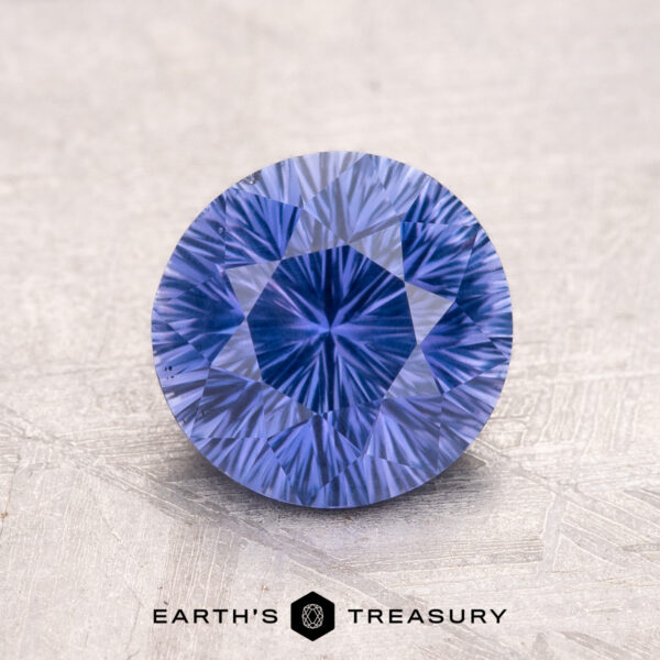 2.05-Carat Ceylon Sapphire A 2.05-carat Ceylon Sapphire, round and faceted with a lavender hue, placed on a textured surface.