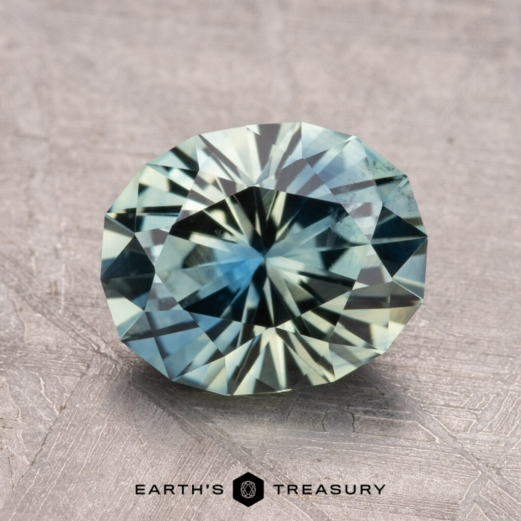 A round, faceted 2.67-carat Montana Sapphire, with a green to blue gradient on a textured surface and branded with the Earth’s Treasury logo at the bottom.