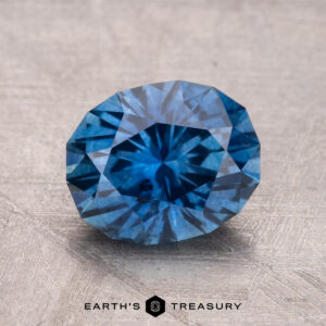 A 2.43-carat Montana Sapphire (heated) in a round brilliant-cut displayed on a textured surface with the logo "Earth's Treasury" beneath.