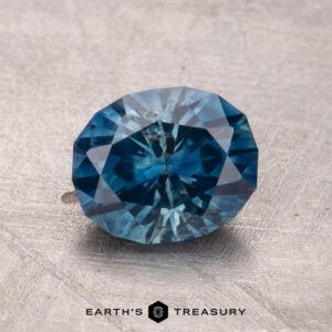 A 2.13-carat heated Montana sapphire displayed on a textured surface with the text "Earth's Treasury" below.