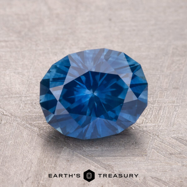 2.10-Carat Montana Sapphire (Heated) A blue, faceted 2.10-carat Montana sapphire (heated) rests on a textured surface with "Earth's Treasury" written below.
.