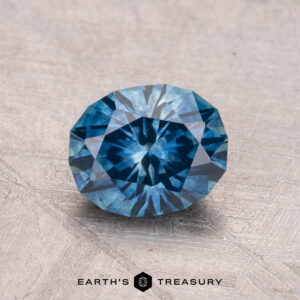 A 1.41-carat Montana Sapphire (Heated) with a brilliant cut and symmetrical geometric pattern rests on a textured surface.