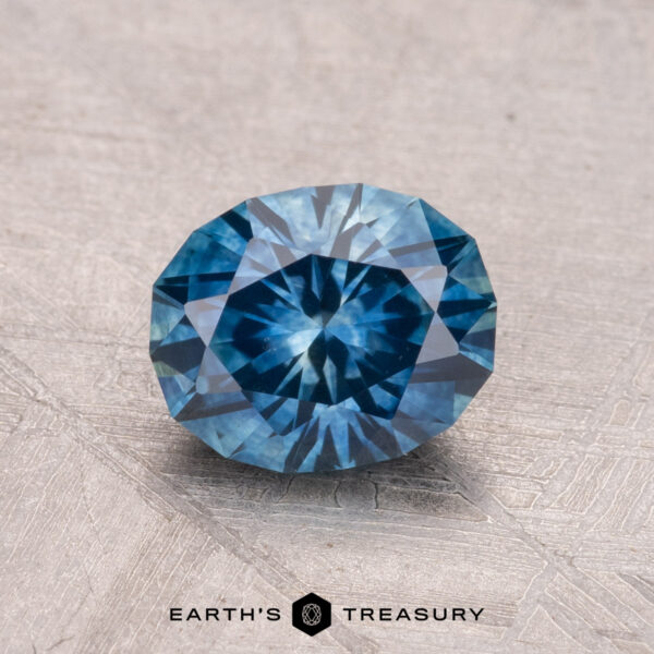 1.41-Carat Montana Sapphire (Heated) A 1.41-carat Montana Sapphire (Heated) with a brilliant cut and symmetrical geometric pattern rests on a textured surface.