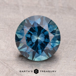 A 2.65-carat heated Montana sapphire on a textured surface, showcasing blue and green hues.