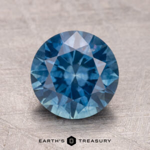A 2.55-carat heated Montana sapphire, with a faceted surface, rests on a textured beige background.