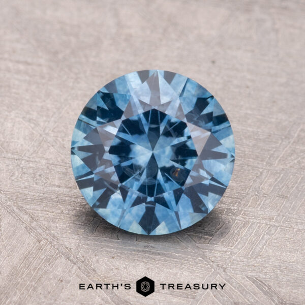 1.66-Carat Montana Sapphire (Heated) A 1.66-carat Montana sapphire (heated) with a round brilliant cut rests on a textured surface.
