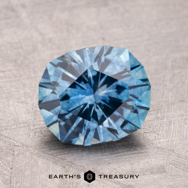 2.30-Carat Montana Sapphire (Heated) A faceted 2.30-carat heated Montana sapphire with a starburst pattern rests on a textured surface. Text at the bottom reads "Earth's Treasury.