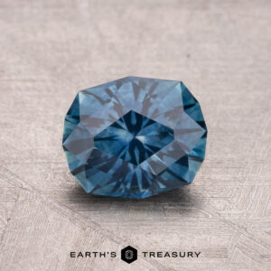 A faceted, round 1.55-carat heated Montana sapphire with a geometric pattern rests on a textured surface.