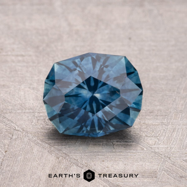 1.55-Carat Montana Sapphire (Heated) A faceted, round 1.55-carat heated Montana sapphire with a geometric pattern rests on a textured surface.