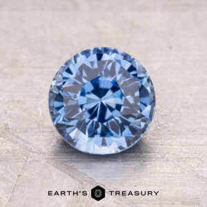 A 1.62-carat Ceylon Sapphire, round and faceted, is showcased on a textured surface.