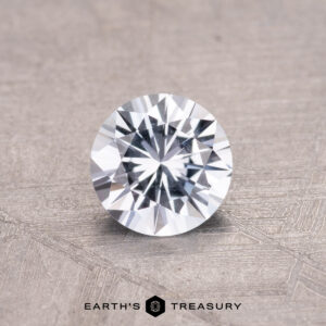 A 0.66-carat Montana sapphire with intricate facets rests on a textured gray surface.