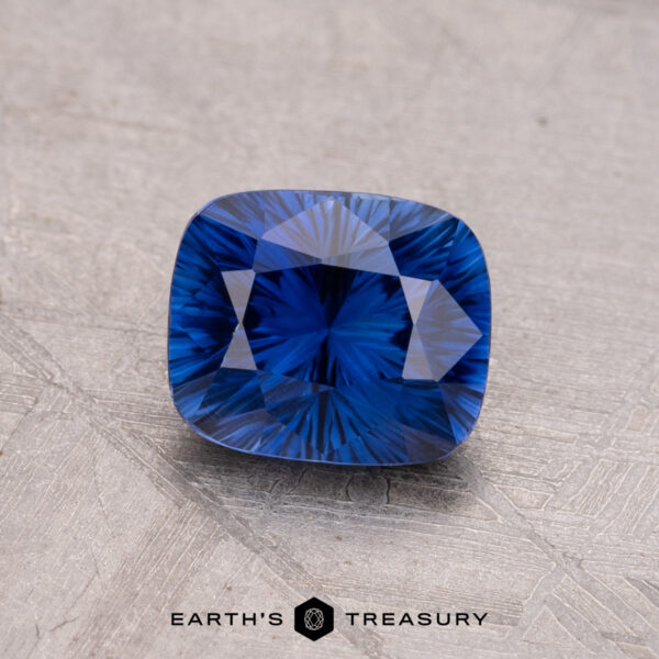 1.32-Carat Ceylon Sapphire (Heated) A 1.32-carat Ceylon sapphire, heated and geometric cut, rests on a textured gray surface with "Earth's Treasury" displayed at the bottom.